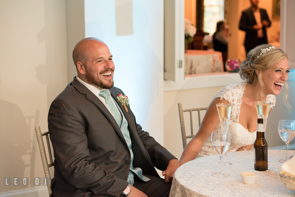 The Oaks Waterfront Inn Bride and Groom at sweetheart table laughing to Maid of Honor and Best Man's toast speeches photo by Leo Dj Photography