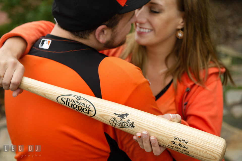 Girl embracing her fiance while holding Baltimore Orioles Louisville Slugger baseball bat. Eastern Shore Maryland pre-wedding engagement photo session at St Michaels MD, by wedding photographers of Leo Dj Photography. http://leodjphoto.com