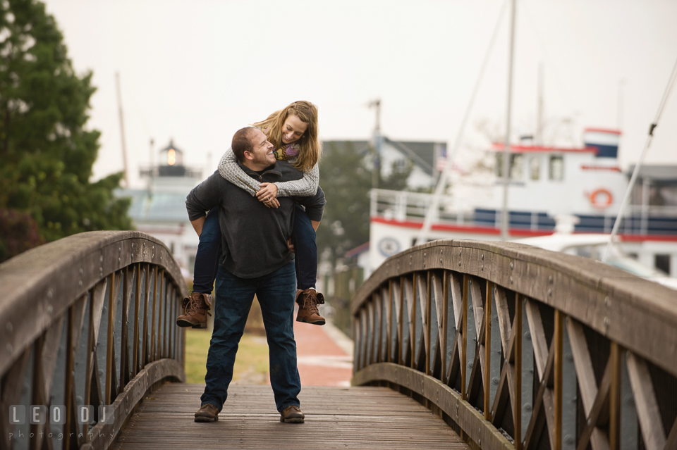 Engaged man carrying his fiancee on his back while walking on the bridge by the boat dock marina. Eastern Shore Maryland pre-wedding engagement photo session at St Michaels MD, by wedding photographers of Leo Dj Photography. http://leodjphoto.com