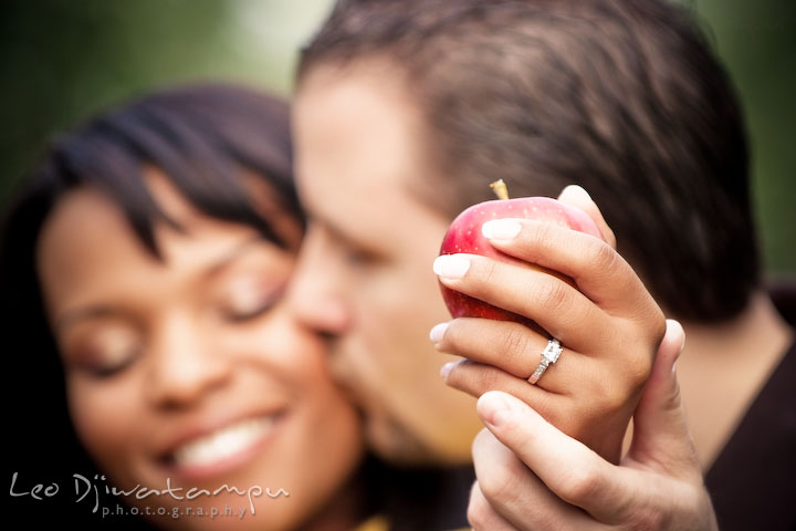 Engaged couple holding apple showing engagement ring, kissing. Engagement pre-wedding photo session fruit tree farm barn flower garden by Leo Dj Photography