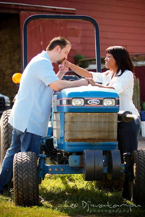 Engaged man kissed fiancee's hand by a blue farm tractor. Engagement pre-wedding photo session fruit tree farm barn flower garden by Leo Dj Photography