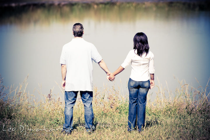 Engaged man and woman holding hands looking at the blue pond. Engagement pre-wedding photo session fruit tree farm barn flower garden by Leo Dj Photography