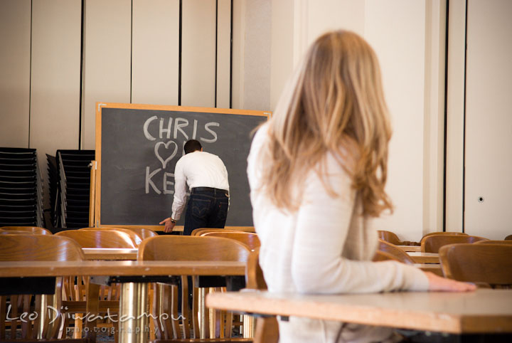 Engaged girl looking at her fiance, writing on blackboard. Pre-wedding engagement photo session at Washington College and Chestertown, Maryland, by wedding photographer Leo Dj Photography.