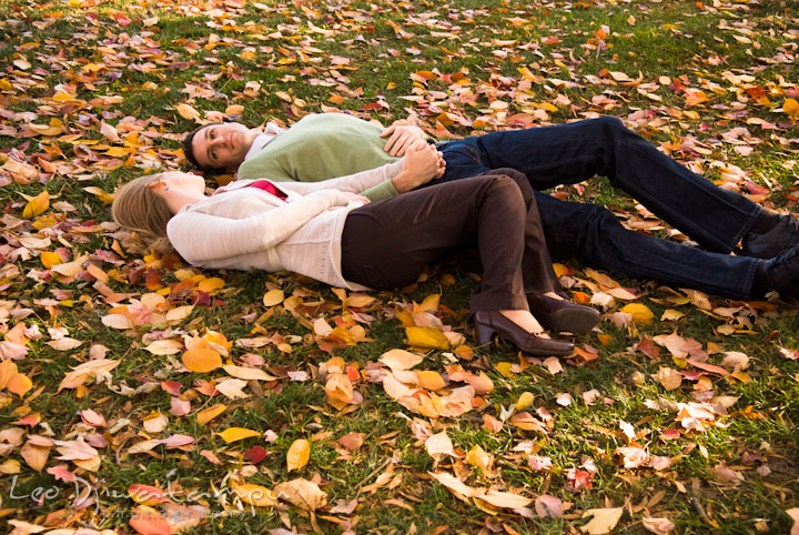 Engaged girl lying on ground filled with fall leaves with his fiancé. Pre-wedding engagement photo session at Washington College and Chestertown, Maryland, by wedding photographer Leo Dj Photography.