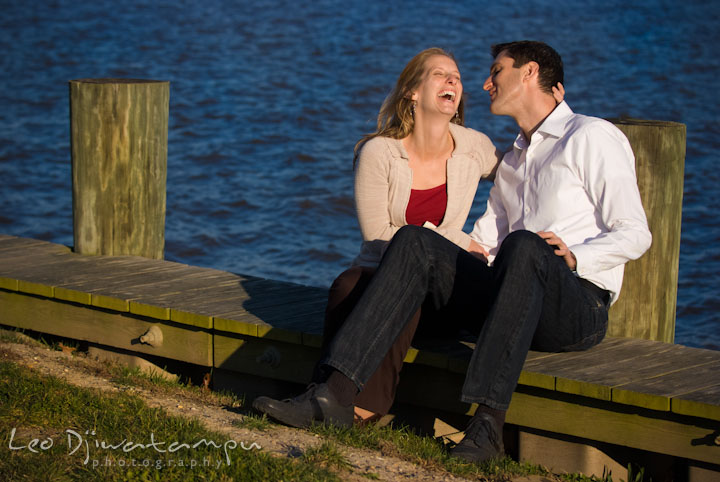 Engaged couple sitting by the pier laughing. Pre-wedding engagement photo session at Washington College and Chestertown, Maryland, by wedding photographer Leo Dj Photography.