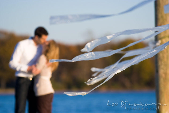 Engaged couple kissing in the background. Pre-wedding engagement photo session at Washington College and Chestertown, Maryland, by wedding photographer Leo Dj Photography.