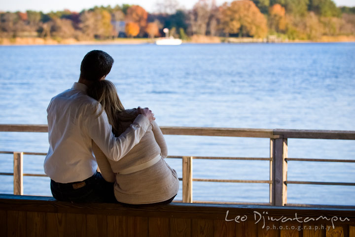 Engaged couple cuddling, looking at the water scenery view. Pre-wedding engagement photo session at Washington College and Chestertown, Maryland, by wedding photographer Leo Dj Photography.