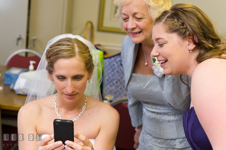 Bride, Mother of Bride and Bridesmaid smiling looking at picture on iPhone. St Andrews United Methodist wedding photos at Annapolis, Eastern Shore, Maryland by photographers of Leo Dj Photography.