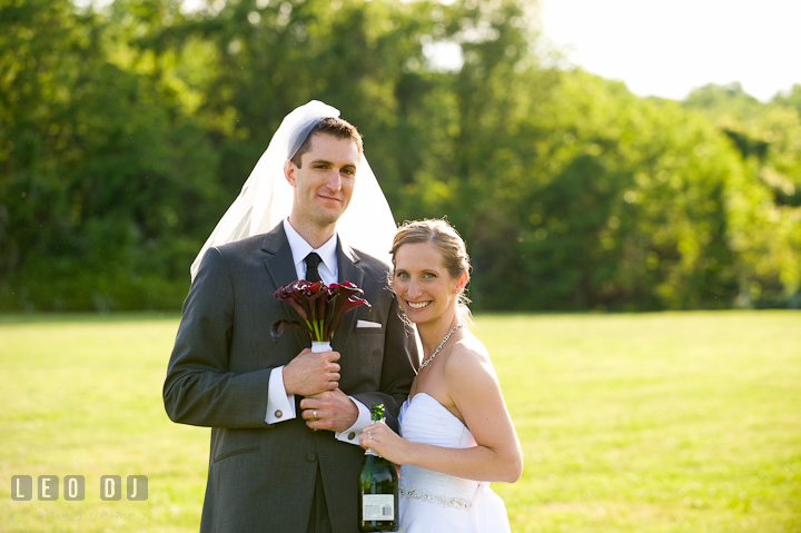 Bride holding champagne bottle. Groom holding bouquet and wearing bride's veil. St Andrews United Methodist wedding photos at Annapolis, Eastern Shore, Maryland by photographers of Leo Dj Photography.