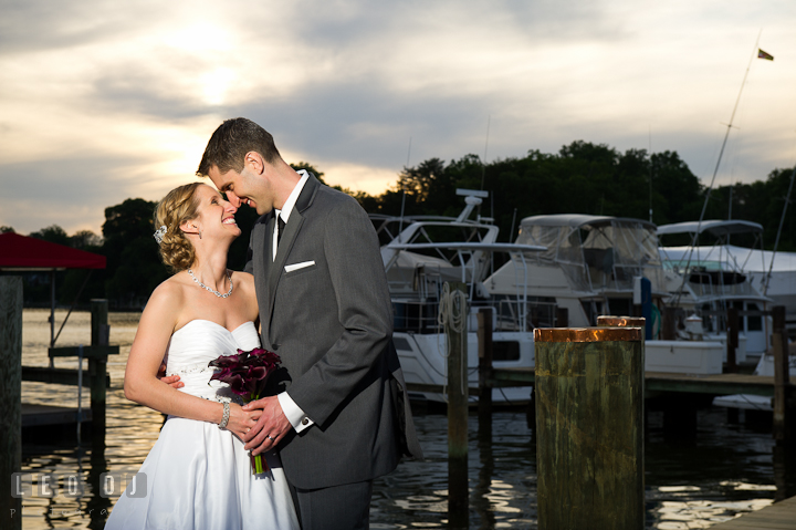 Bride and Groom cuddling and smiling together at boat docks during sunset. Yellowfin Restaurant wedding reception photos at Annapolis, Eastern Shore, Maryland by photographers of Leo Dj Photography.