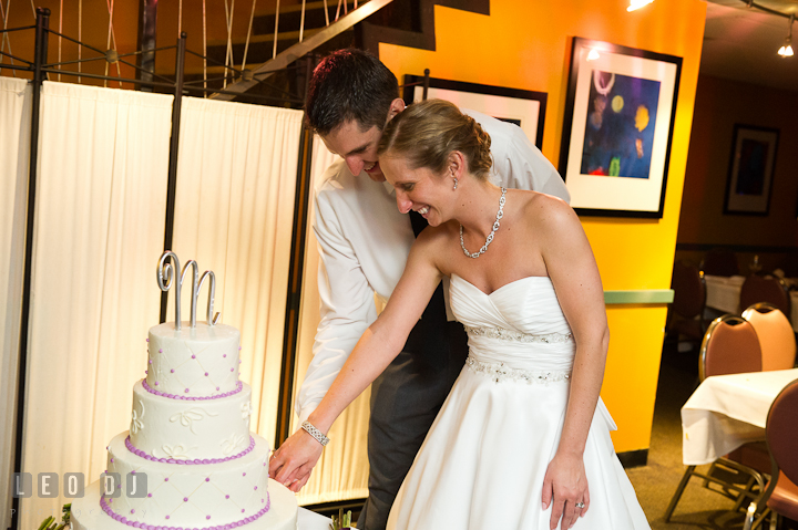 Bride and Groom smiling while cutting cake. Yellowfin Restaurant wedding reception photos at Annapolis, Eastern Shore, Maryland by photographers of Leo Dj Photography.