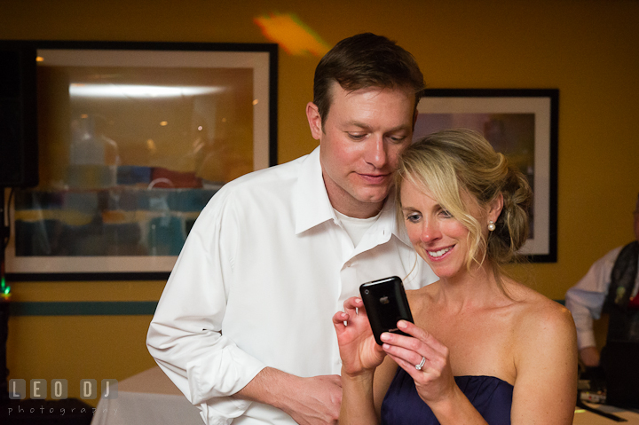 Brother of Bride and his wife looking at pictures on their phone. Yellowfin Restaurant wedding reception photos at Annapolis, Eastern Shore, Maryland by photographers of Leo Dj Photography.