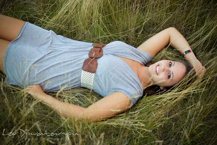 Girl laying on grass in a tall grass field. Eastern Shore, Maryland, Kent Island High School senior portrait session by photographer Leo Dj Photography.