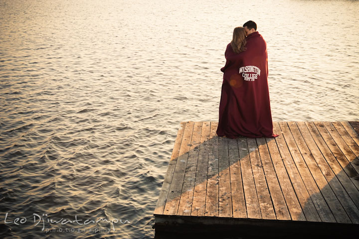 Fiancé and his fiancée cuddling on a pier with a college blanket. Chestertown Maryland and Washington College Pre-Wedding Engagement Session Photographer, Leo Dj Photography