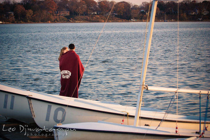 Engaged couple cuddling on a sailboat pier with a college blanket. Chestertown Maryland and Washington College Pre-Wedding Engagement Session Photographer, Leo Dj Photography