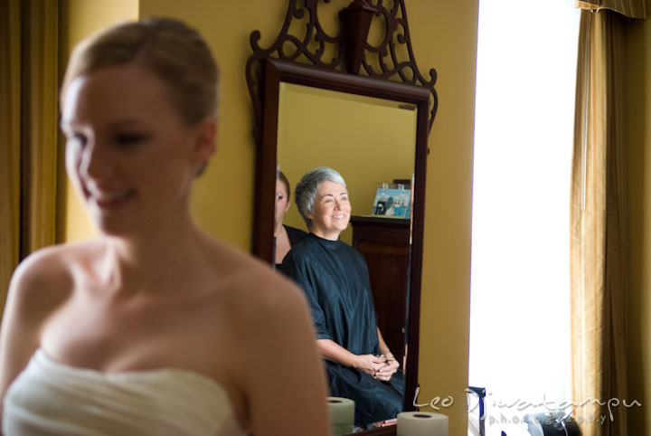 Mother of groom's reflection on mirror while watching bride putting on her dress. The Tidewater Inn Wedding, Easton Maryland, getting ready photo coverage of Kelsey and Jonnie by wedding photographers of Leo Dj Photography.