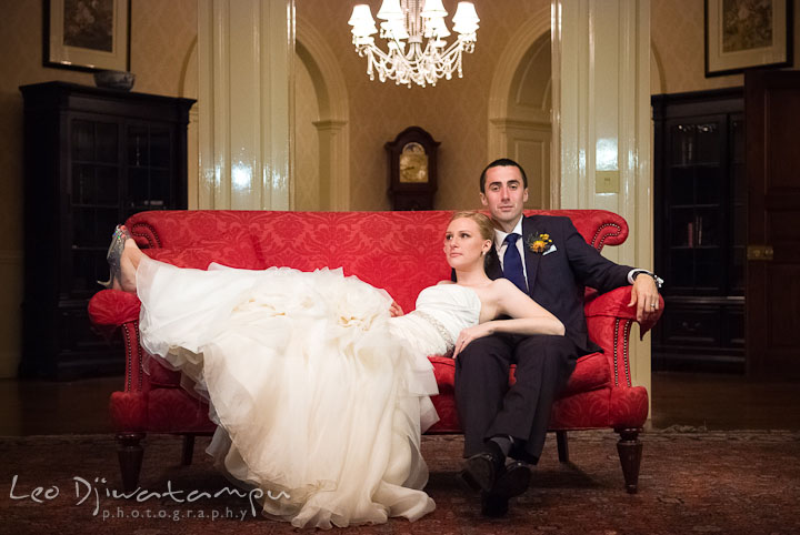 Bride and groom posing on a red antique sofa. The Tidewater Inn Wedding, Easton Maryland, reception photo coverage of Kelsey and Jonnie by wedding photographers of Leo Dj Photography.