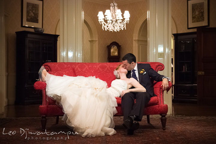 Bride and groom kissing on red antique sofa. The Tidewater Inn Wedding, Easton Maryland, reception photo coverage of Kelsey and Jonnie by wedding photographers of Leo Dj Photography.