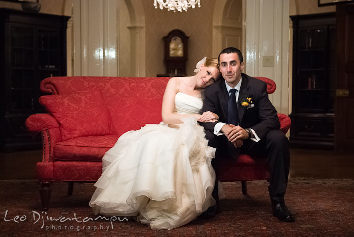 Bride sitting on red antique couch and leaning on groom's shoulder. The Tidewater Inn Wedding, Easton Maryland, reception photo coverage of Kelsey and Jonnie by wedding photographers of Leo Dj Photography.