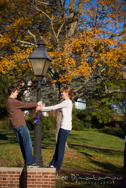 Engaged guy and girl playing by a light pole. Pre-wedding engagement photo session at Washington College and Chestertown, Maryland, by wedding photographer Leo Dj Photography.