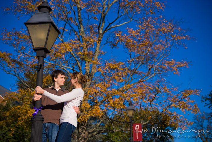 Engaged couple embracing by a light pole. Pre-wedding engagement photo session at Washington College and Chestertown, Maryland, by wedding photographer Leo Dj Photography.