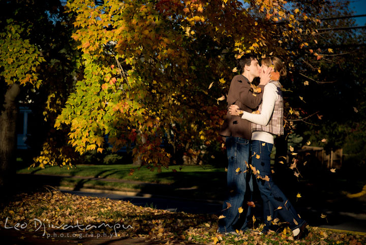 Engaged guy and girl kissing under a tree with falling leaves. Pre-wedding engagement photo session at Washington College and Chestertown, Maryland, by wedding photographer Leo Dj Photography.