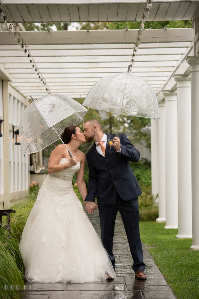 Chesapeake Bay Beach Club Bride and Groom with umbrella kissing under the rain photo by Leo Dj Photography.