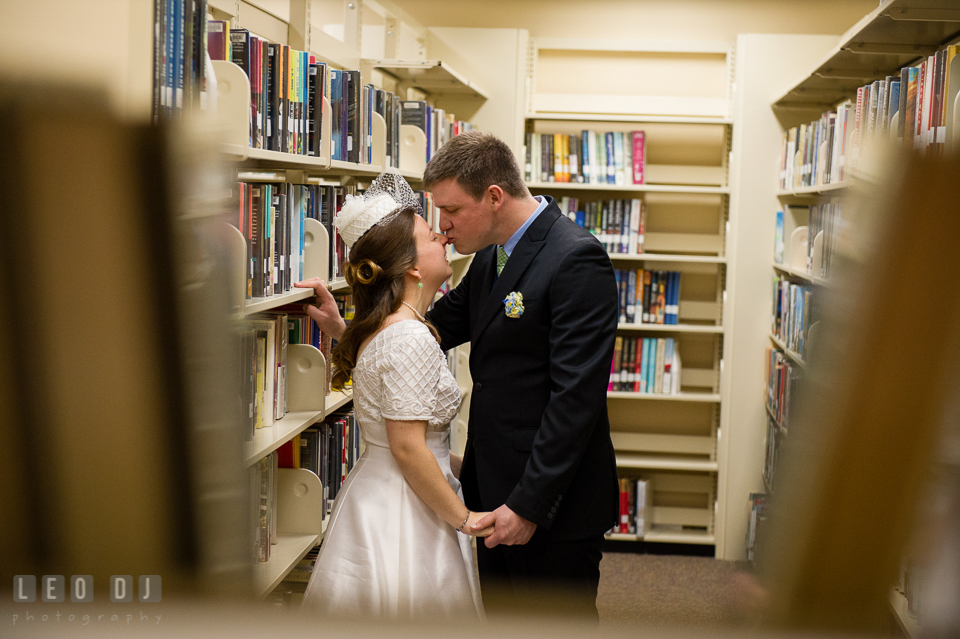 Groom kissing Bride in between rows of book shelves in the library. Fisherman's Inn, Safe Harbor Church, Kent Island, Eastern Shore Maryland, wedding reception and ceremony photo, by wedding photographers of Leo Dj Photography. http://leodjphoto.com