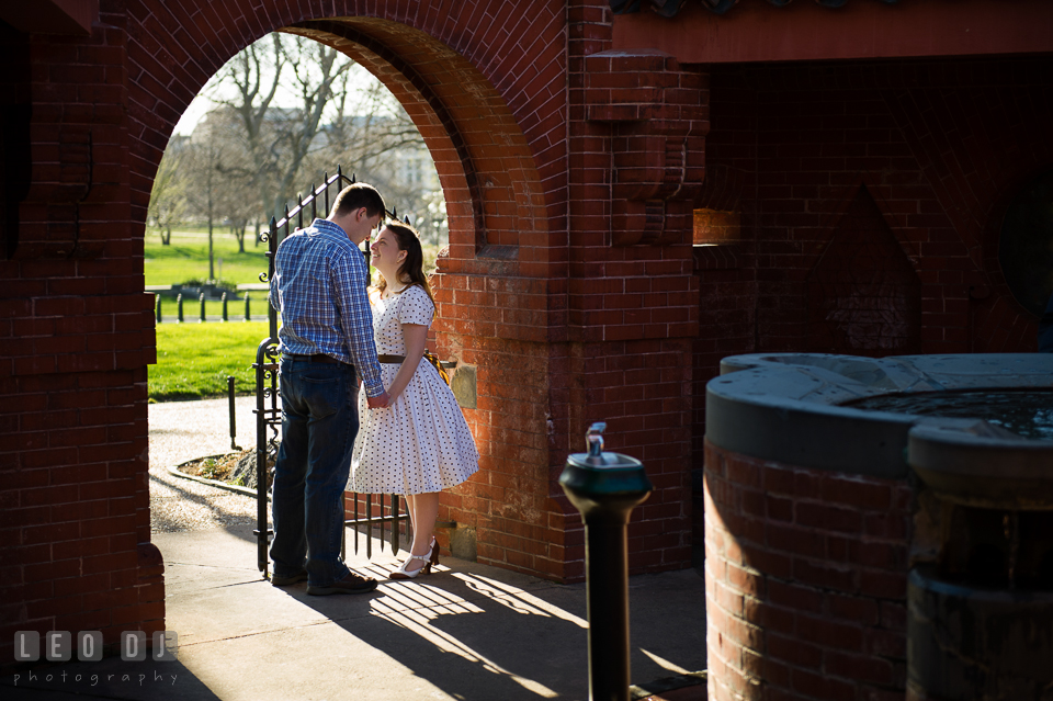 Engaged couple holding hands by a gate at the Summerhouse structure. Washington DC pre-wedding engagement photo session at the Capitol Hill and the Mall, by wedding photographers of Leo Dj Photography. http://leodjphoto.com