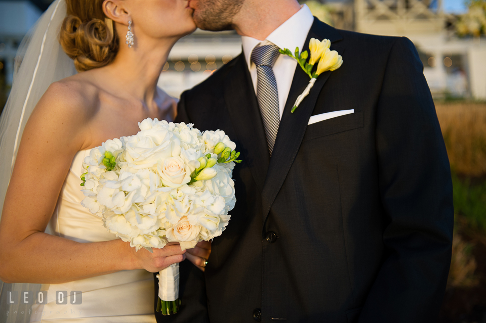 Bride holding her flower bouquet kissing the groom. Kent Island Maryland Chesapeake Bay Beach Club wedding photo, by wedding photographers of Leo Dj Photography. http://leodjphoto.com