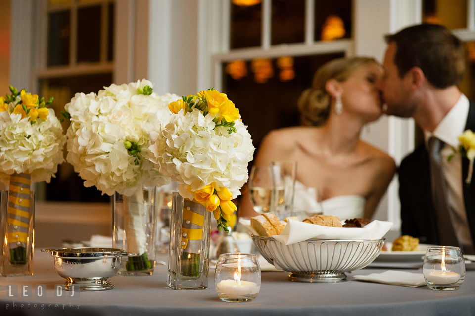 Sweetheart table with the flower bouquets with the Bride and Groom kissing in the background. Kent Island Maryland Chesapeake Bay Beach Club wedding photo, by wedding photographers of Leo Dj Photography. http://leodjphoto.com