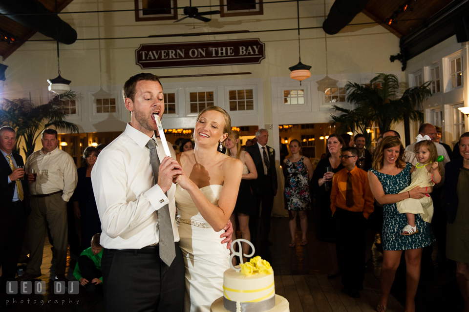 Groom licking cake icing from knife during cake cutting. Kent Island Maryland Chesapeake Bay Beach Club wedding photo, by wedding photographers of Leo Dj Photography. http://leodjphoto.com