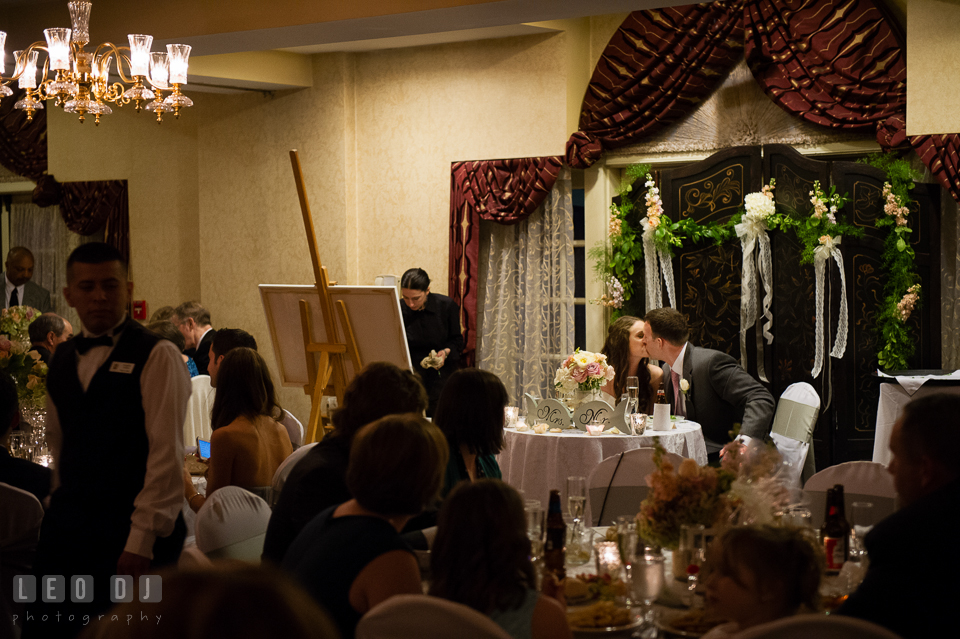 Bride and Groom kissing at their sweetheart table after glass clinking from guests while the painter Patricia Bennet paints the room. Historic Inns of Annapolis Maryland, Governor Calvert House wedding, by wedding photographers of Leo Dj Photography. http://leodjphoto.com