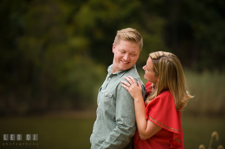 Engaged girl hugging her fiancé from behind, smiling and looking at each other. Chestertown Eastern Shore Maryland pre-wedding engagement photo session by the water, by wedding photographers of Leo Dj Photography. http://leodjphoto.com