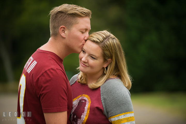 Engaged guy kissing his fiancée, both wearing Washington Redskins football shirt and jersey. Chestertown Eastern Shore Maryland pre-wedding engagement photo session by the water, by wedding photographers of Leo Dj Photography. http://leodjphoto.com