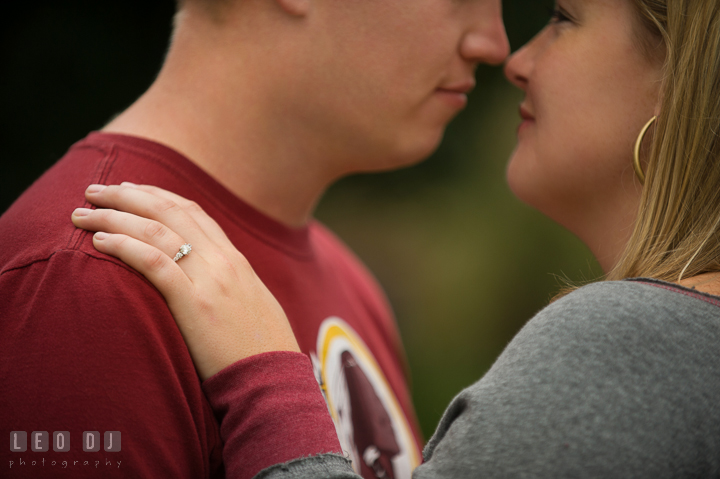 Engaged girl cuddling with her fiancé showing her engagement ring, wearing Washington Redskins football shirt and jersey. Chestertown Eastern Shore Maryland pre-wedding engagement photo session by the water, by wedding photographers of Leo Dj Photography. http://leodjphoto.com