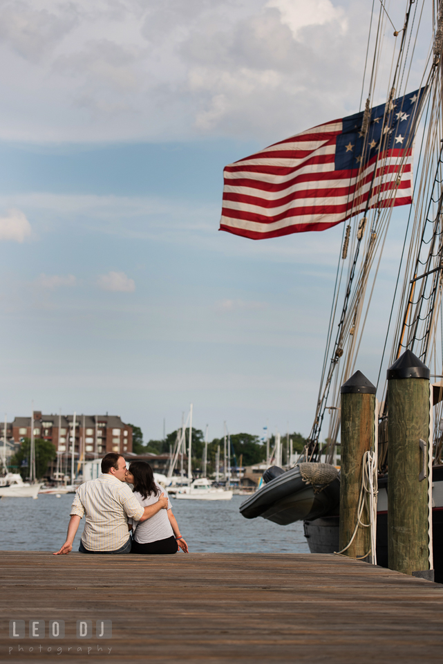 Engaged couple kissing on the dock with vintage American flag from a tall ship. Annapolis Eastern Shore Maryland pre-wedding engagement photo session at downtown, by wedding photographers of Leo Dj Photography. http://leodjphoto.com