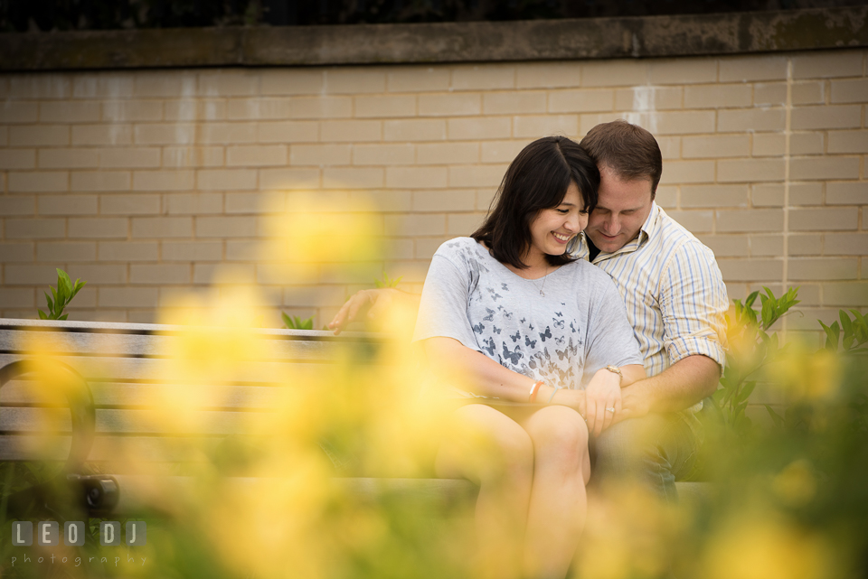 Engaged girl sitting on bench and cuddling together with her fiance. Annapolis Eastern Shore Maryland pre-wedding engagement photo session at downtown, by wedding photographers of Leo Dj Photography. http://leodjphoto.com