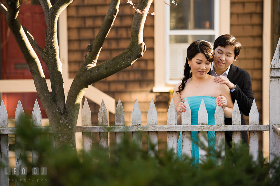 Romantic engaged couple embracing by a picket fence. Annapolis Eastern Shore Maryland pre-wedding engagement photo session at downtown, by wedding photographers of Leo Dj Photography. http://leodjphoto.com