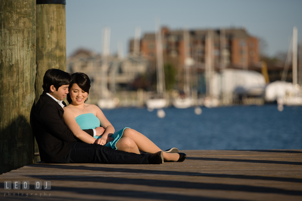 Engaged girl sitting on the dock and embraced by her fiance. Annapolis Eastern Shore Maryland pre-wedding engagement photo session at downtown, by wedding photographers of Leo Dj Photography. http://leodjphoto.com