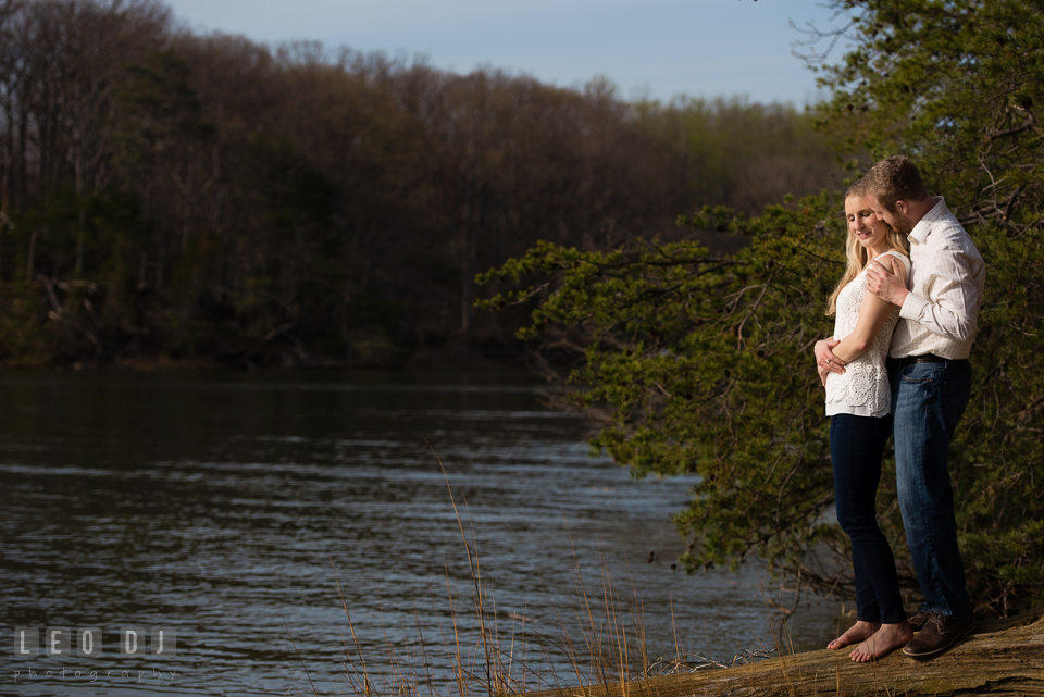 Engaged man hugging his fiancé by the river. Quiet Waters Park Annapolis Maryland pre-wedding engagement photo session, by wedding photographers of Leo Dj Photography. http://leodjphoto.com
