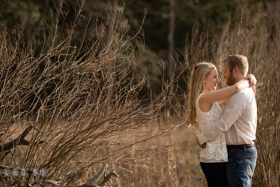 Engaged man and his fiancee embracing each other by the woods. Quiet Waters Park Annapolis Maryland pre-wedding engagement photo session, by wedding photographers of Leo Dj Photography. http://leodjphoto.com