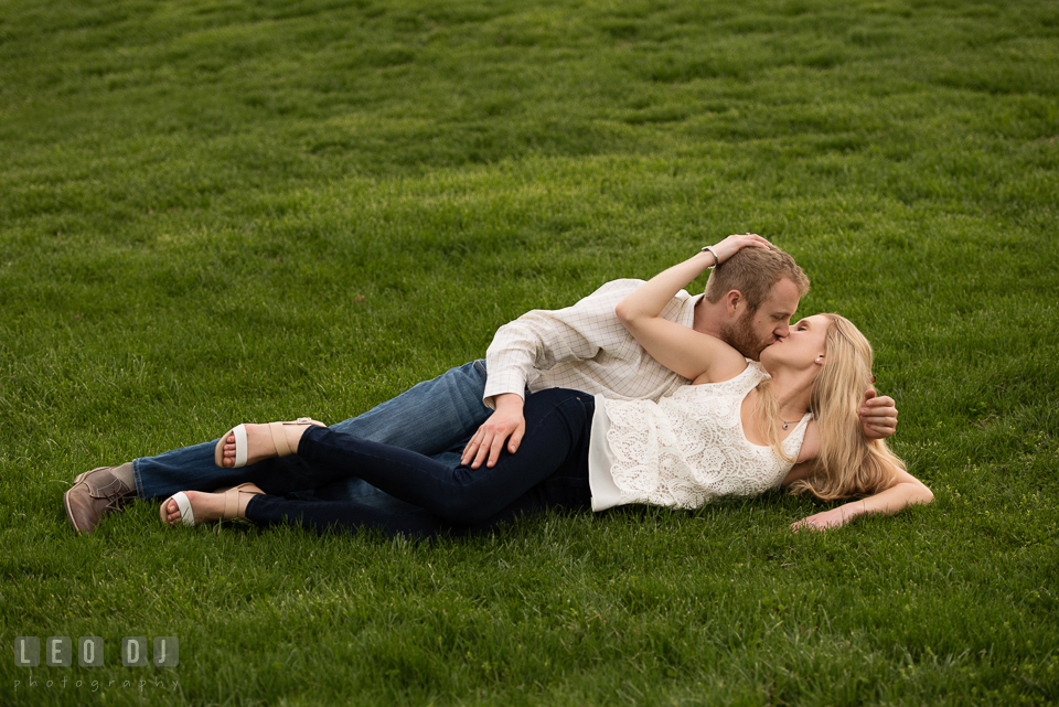 Engaged guy and his fiancee laying on the grass kissing. Quiet Waters Park Annapolis Maryland pre-wedding engagement photo session, by wedding photographers of Leo Dj Photography. http://leodjphoto.com