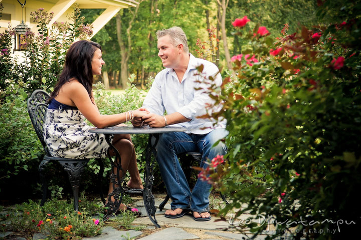engaged couple sitting by a rose flower garden. guy holding his fiancee. Kent Island, Eastern Shore, Maryland Engagement Pre-wedding photography session
