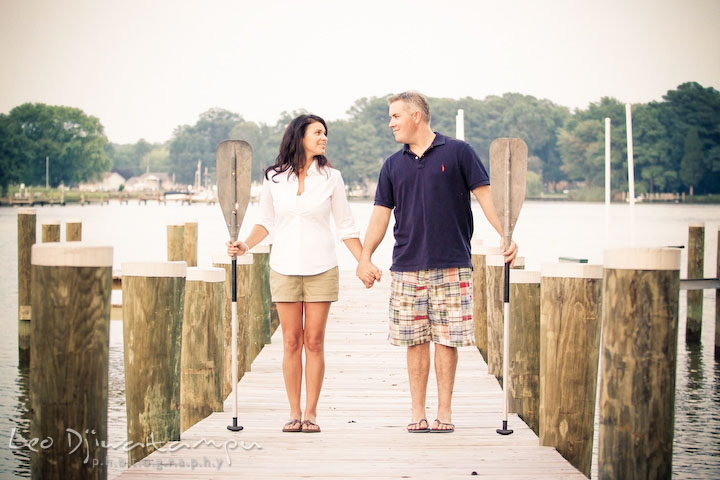a girl and her fiancee holding boat paddle and standing on pier. Kent Island, Eastern Shore, Maryland Engagement Pre-wedding photography session