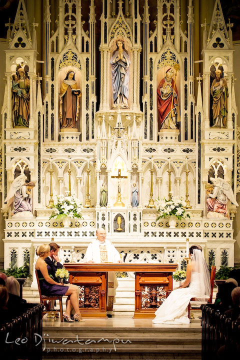 Bride, groom, maid of honor, best man, and priest at the ceremony with the beautiful church interior in the background. Annapolis Wedding Photographer, Wedding at St Mary's Catholic Church Annapolis Maryland.