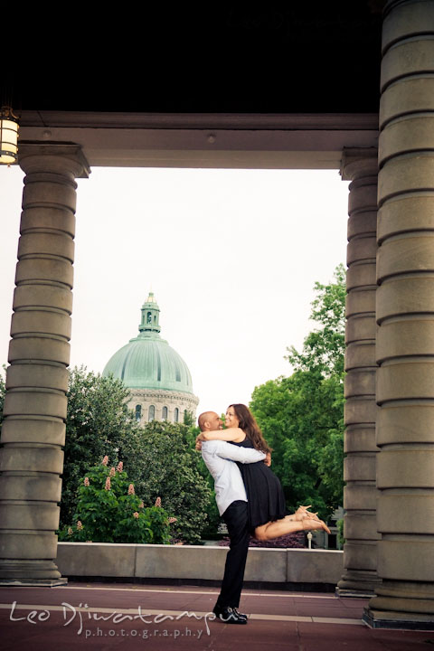 Engaged guy lifted up his fiancée, laughing. US Naval Academy chapel dome in the background. Annapolis Maryland USNA Pre-Wedding Engagement Photo Session by wedding photographer Leo Dj Photography