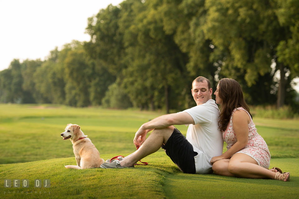 Engaged man lounging on the grass with his dog and fiancee. Leesburg Virginia pre-wedding engagement photo session at River Creek Club, by wedding photographers of Leo Dj Photography. http://leodjphoto.com