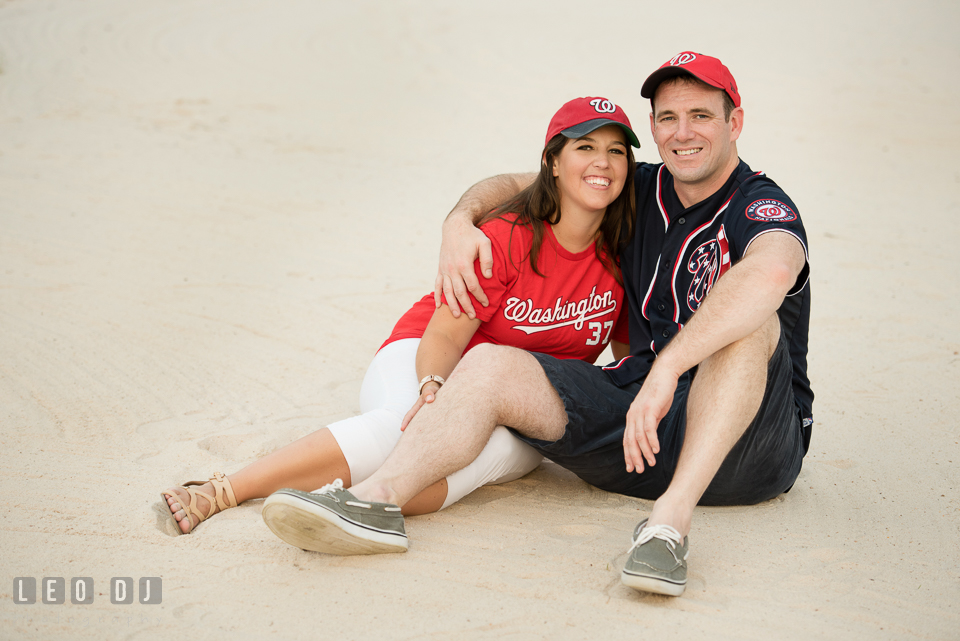 Engaged couple with MLB Washington Nationals jersey and cap lounging on the white sand. Leesburg Virginia pre-wedding engagement photo session at River Creek Club, by wedding photographers of Leo Dj Photography. http://leodjphoto.com