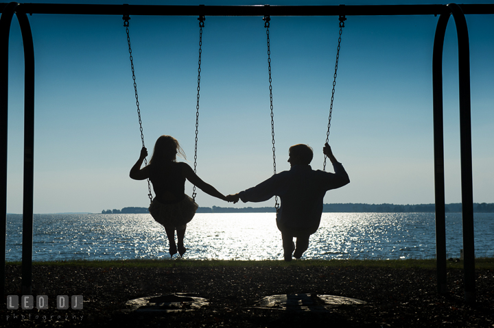 Silhouette of engaged girl playing swing with her fiancé. Oxford, Eastern Shore Maryland pre-wedding engagement photo session, by wedding photographers of Leo Dj Photography. http://leodjphoto.com